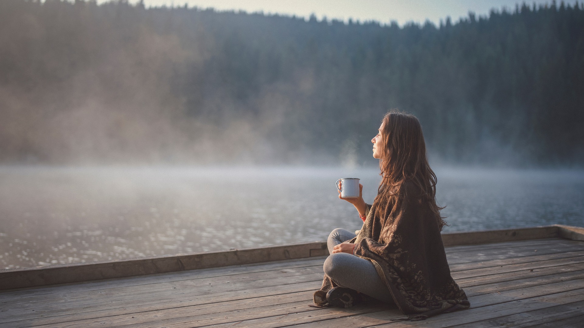 A woman sitting near water holding a mug outside